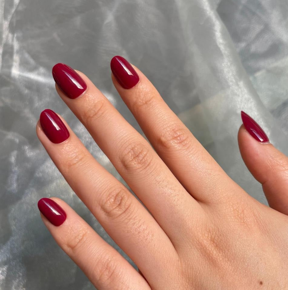 Hand with almond-shaped glossy berry-red press-on nails in natural lighting, wearing a white shirt